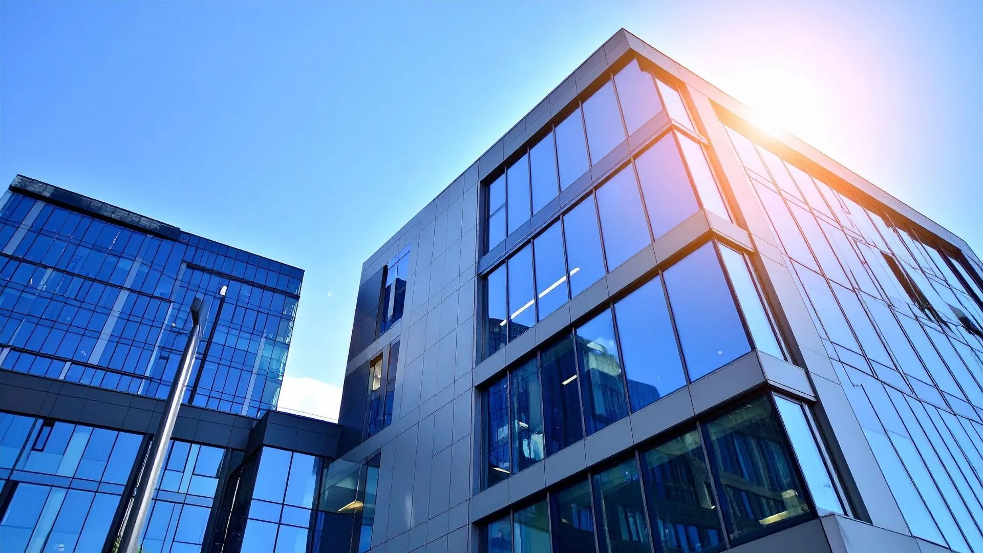 Sunlit glass building corner against blue sky