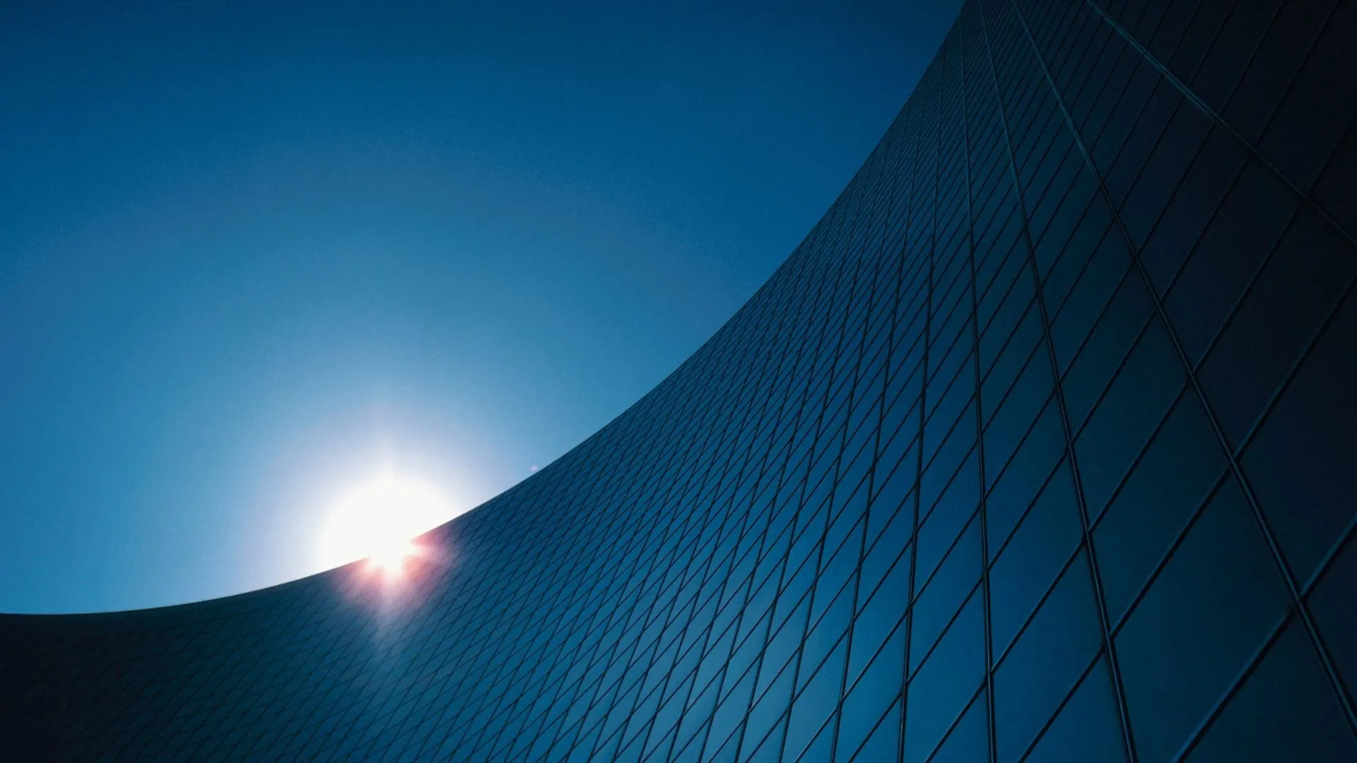 Upward view of a navy-toned glass tower facade with a lens flare
