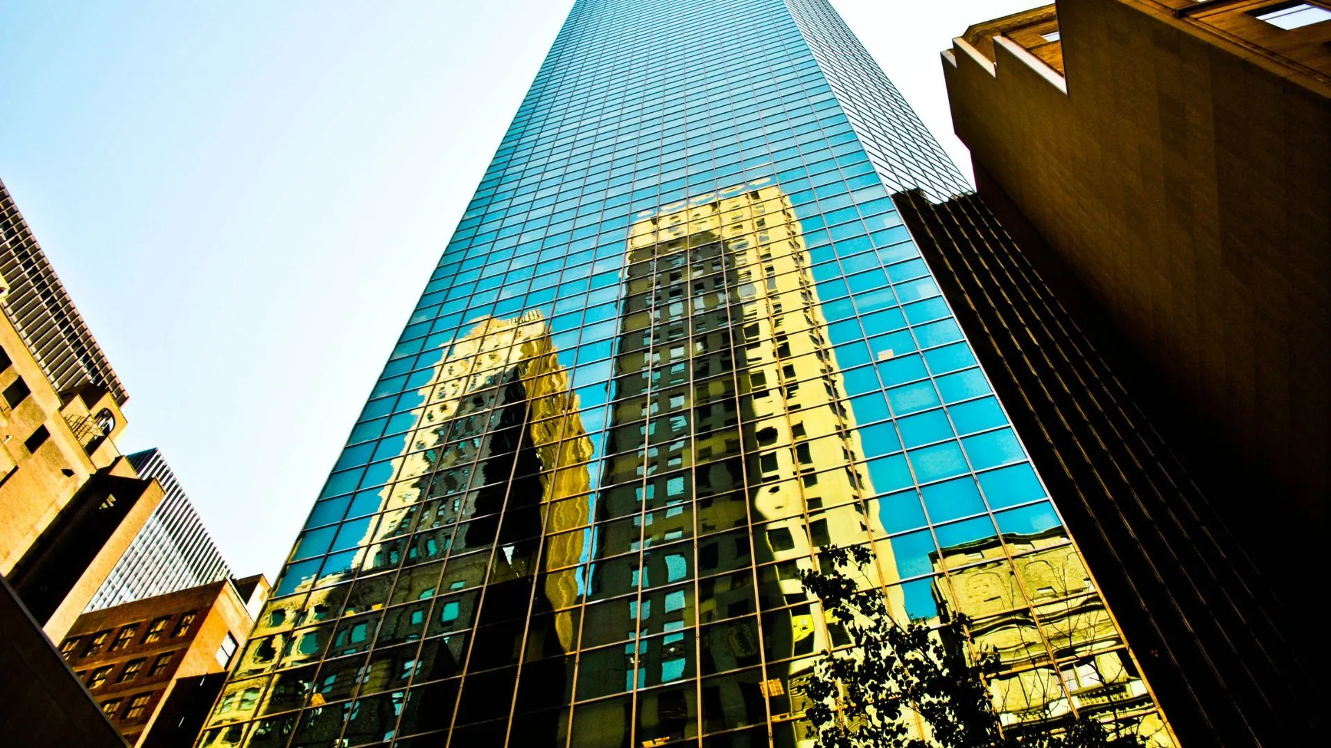 Upward view of a blue glass tower reflecting a nearby building against copper-toned neighboring facades